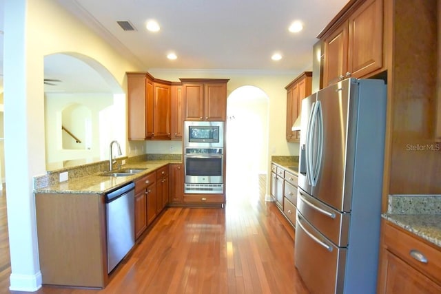 kitchen featuring stainless steel appliances, sink, ornamental molding, light stone countertops, and dark wood-type flooring