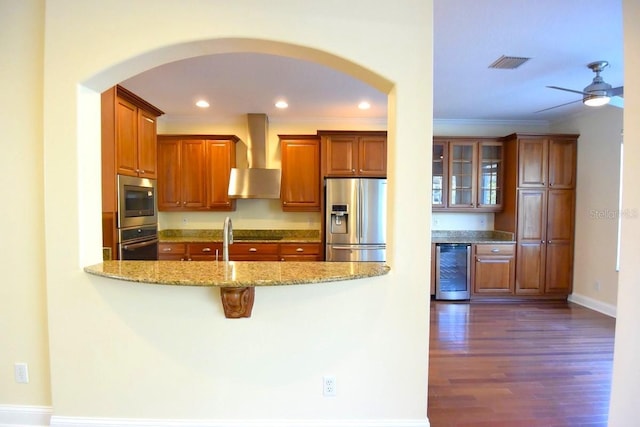 kitchen with light stone counters, wall chimney exhaust hood, ornamental molding, beverage cooler, and appliances with stainless steel finishes