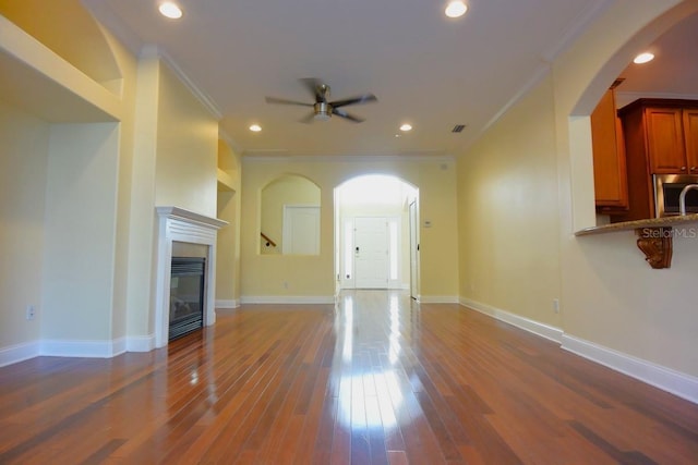 unfurnished living room featuring ceiling fan, dark hardwood / wood-style flooring, and crown molding