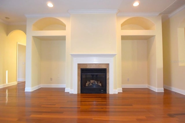 unfurnished living room with built in shelves, a tiled fireplace, crown molding, and dark hardwood / wood-style floors