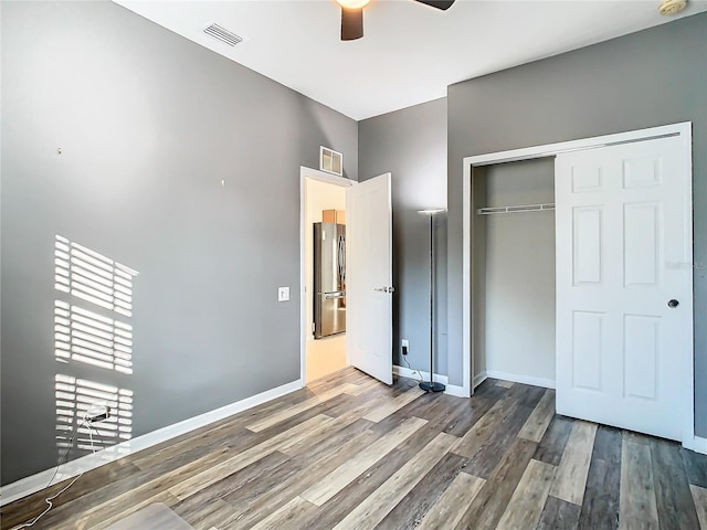 unfurnished bedroom with hardwood / wood-style floors, a closet, stainless steel refrigerator, and ceiling fan