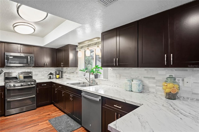 kitchen featuring stainless steel appliances, sink, backsplash, light wood-type flooring, and dark brown cabinets