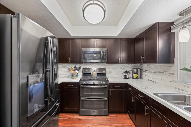 kitchen featuring pendant lighting, wood-type flooring, stainless steel appliances, backsplash, and a raised ceiling