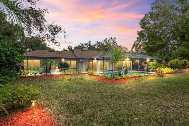 back house at dusk with glass enclosure and a yard