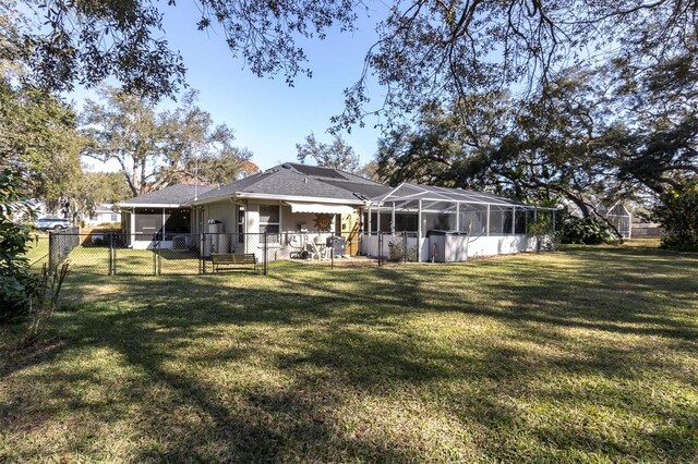 rear view of house with stucco siding, a lawn, a gate, fence, and a sunroom