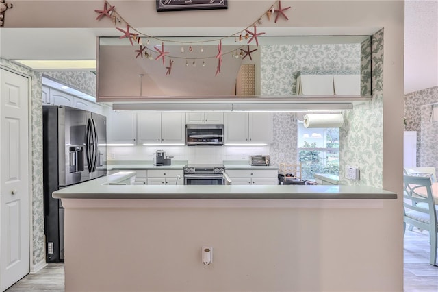 kitchen featuring backsplash, kitchen peninsula, white cabinetry, light wood-type flooring, and appliances with stainless steel finishes