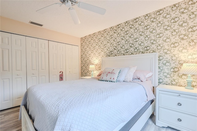 bedroom with a textured ceiling, ceiling fan, a closet, and light hardwood / wood-style flooring