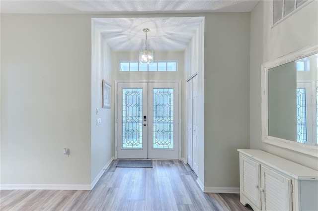 foyer with french doors, a chandelier, and light hardwood / wood-style flooring