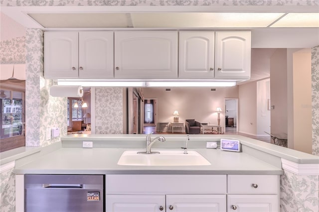 kitchen with stainless steel dishwasher, kitchen peninsula, sink, and white cabinetry