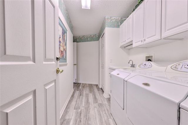 clothes washing area featuring washer and clothes dryer, light wood-type flooring, a textured ceiling, cabinets, and sink