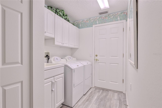 washroom featuring cabinets, a textured ceiling, washing machine and dryer, and light wood-type flooring