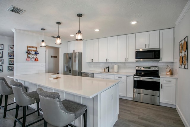 kitchen featuring decorative light fixtures, white cabinets, kitchen peninsula, a breakfast bar area, and appliances with stainless steel finishes