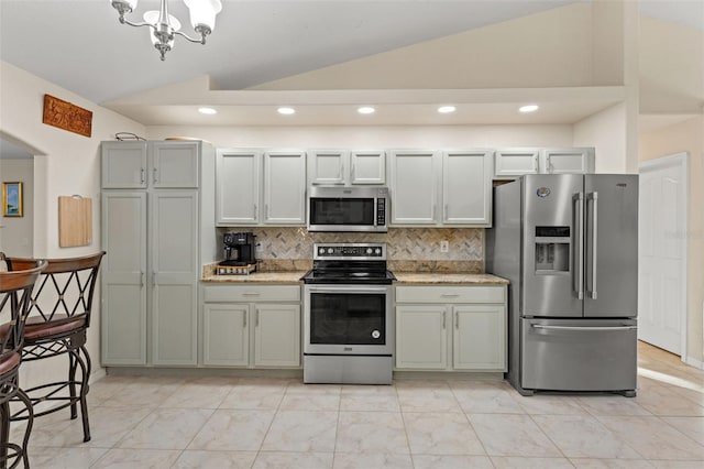 kitchen featuring stainless steel appliances, light stone counters, lofted ceiling, decorative backsplash, and a chandelier