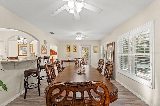 dining space with ceiling fan with notable chandelier and hardwood / wood-style flooring