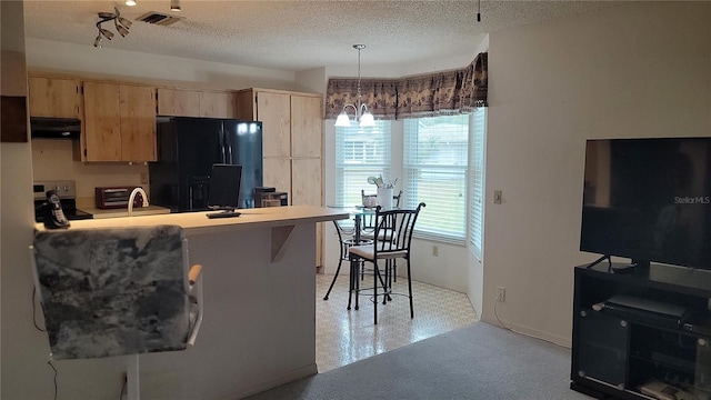 kitchen with a textured ceiling, pendant lighting, black fridge with ice dispenser, and a kitchen bar