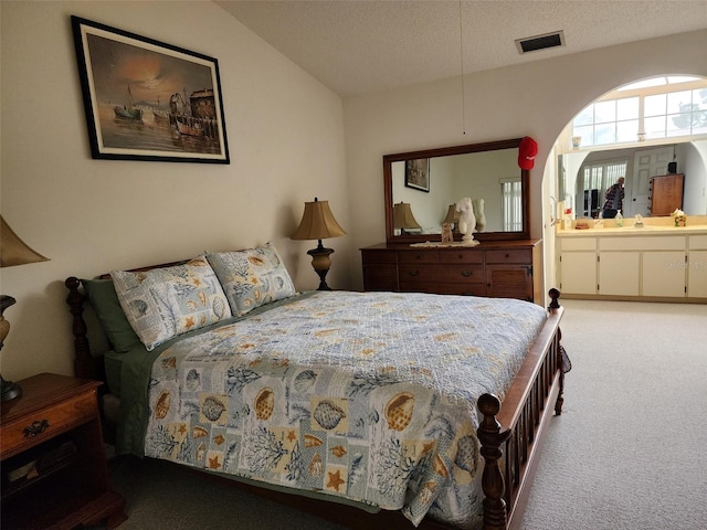 bedroom with ensuite bath, a textured ceiling, and light colored carpet