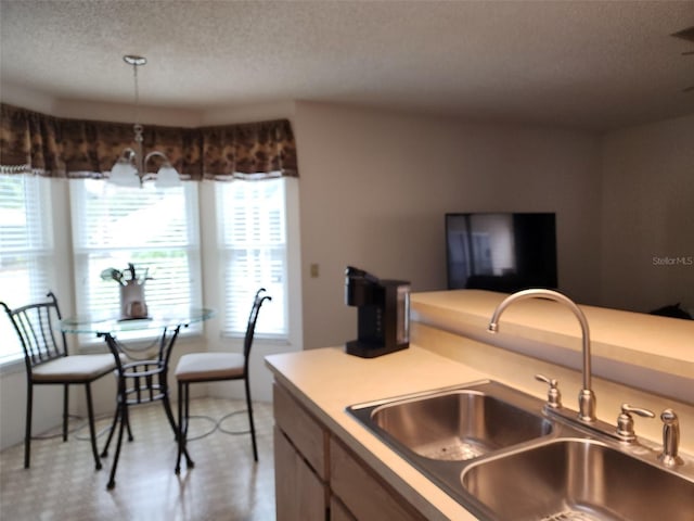 kitchen featuring sink, a textured ceiling, hanging light fixtures, and a notable chandelier