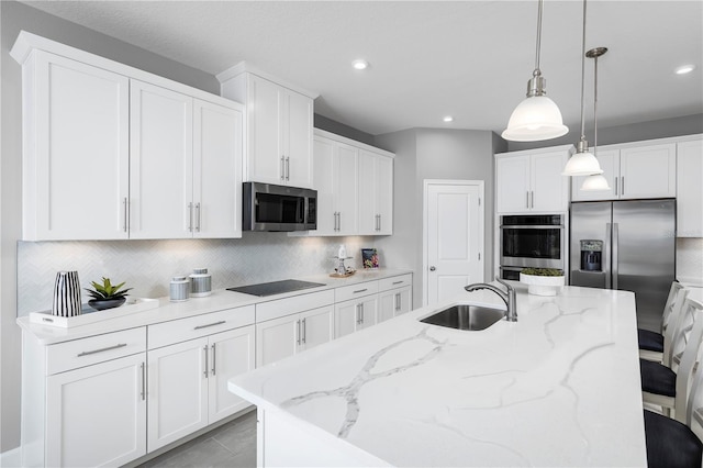 kitchen featuring a center island with sink, appliances with stainless steel finishes, white cabinets, decorative light fixtures, and sink