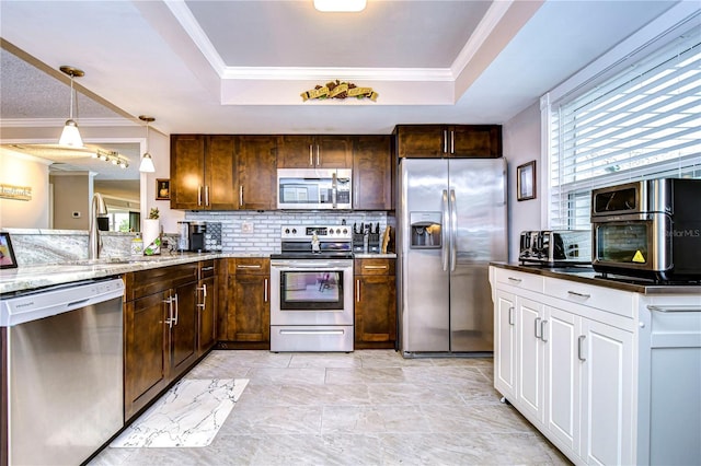 kitchen with light stone countertops, a raised ceiling, appliances with stainless steel finishes, and ornamental molding