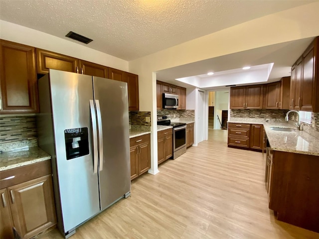 kitchen featuring light hardwood / wood-style flooring, stainless steel appliances, tasteful backsplash, a tray ceiling, and sink