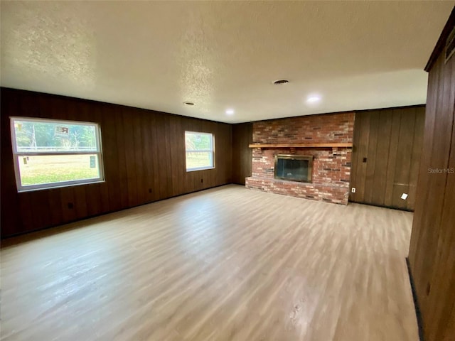 unfurnished living room with a fireplace, a textured ceiling, wood walls, and light wood-type flooring