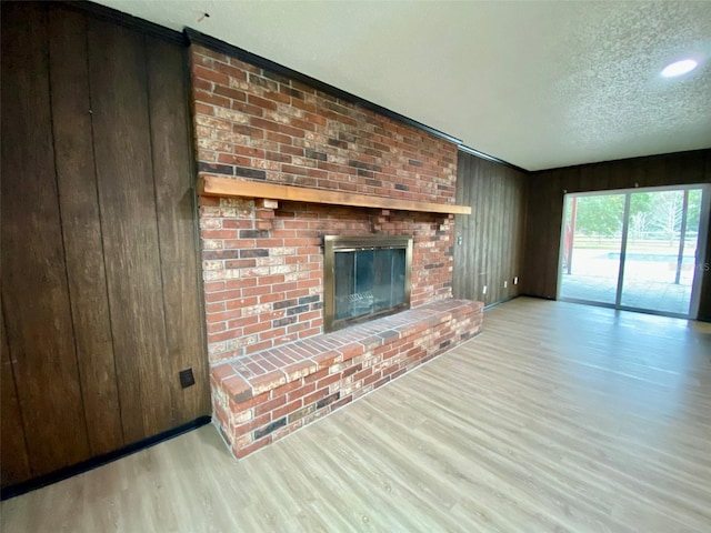 unfurnished living room featuring a brick fireplace, wood walls, a textured ceiling, and light hardwood / wood-style flooring