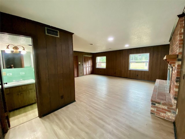 unfurnished living room with sink, light hardwood / wood-style floors, and wooden walls