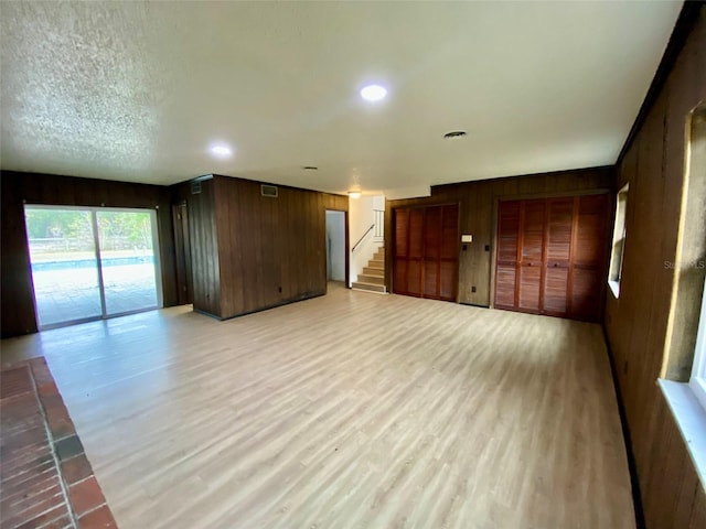 unfurnished living room with a textured ceiling, light hardwood / wood-style flooring, and wood walls