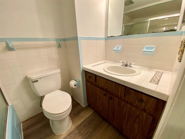 bathroom with tile walls, hardwood / wood-style floors, a shower with shower door, toilet, and vanity