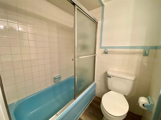 bathroom featuring toilet, combined bath / shower with glass door, tile walls, and hardwood / wood-style floors