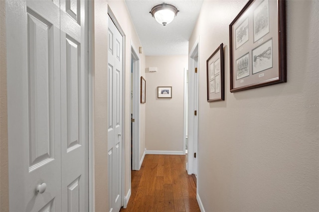 corridor with a textured ceiling and wood-type flooring