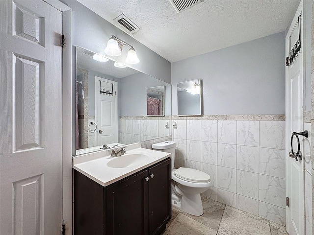 bathroom featuring a textured ceiling, toilet, tile walls, and vanity