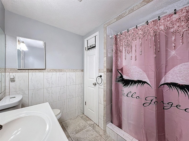 bathroom with curtained shower, tile walls, toilet, and a textured ceiling