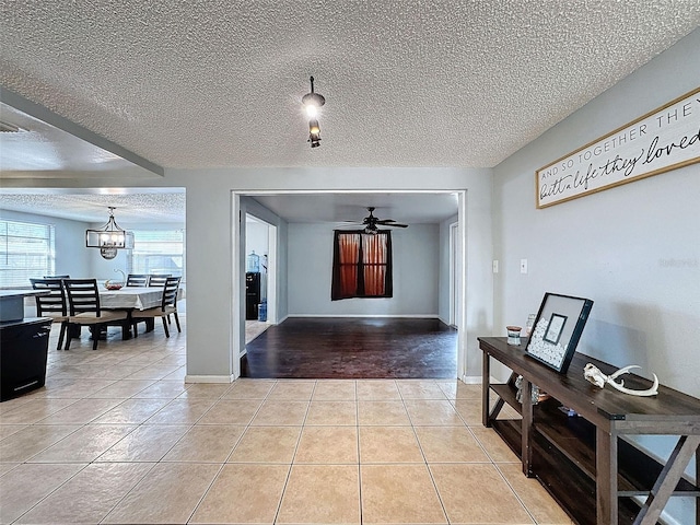 tiled foyer entrance with ceiling fan with notable chandelier and a textured ceiling