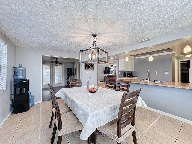 tiled dining room featuring a textured ceiling, ceiling fan with notable chandelier, a tray ceiling, and sink