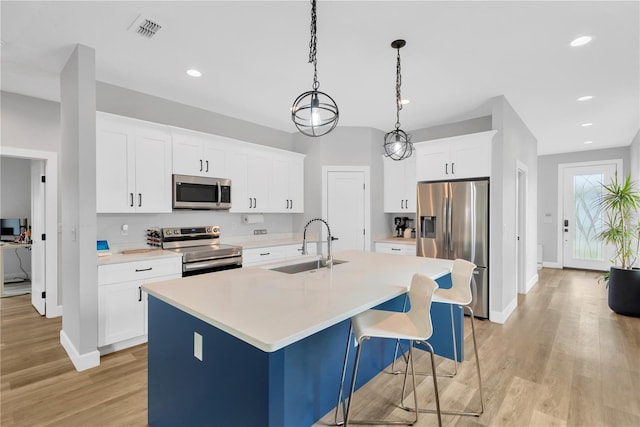 kitchen with stainless steel appliances, sink, white cabinetry, a center island with sink, and pendant lighting