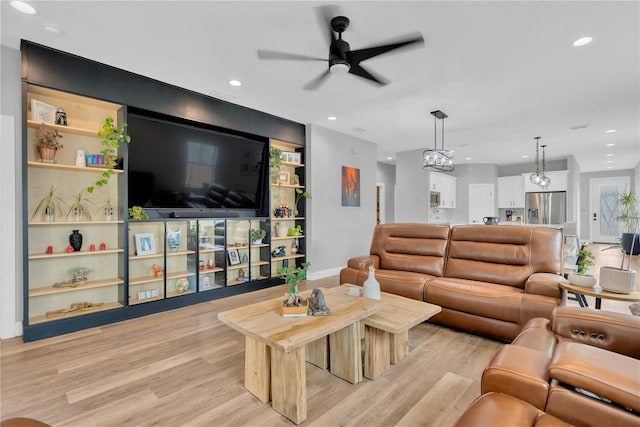 living room with ceiling fan with notable chandelier, built in shelves, and light hardwood / wood-style flooring