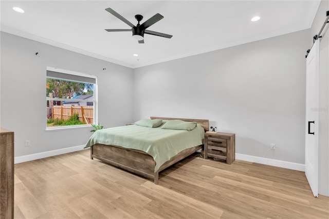 bedroom with crown molding, ceiling fan, a barn door, and light hardwood / wood-style flooring