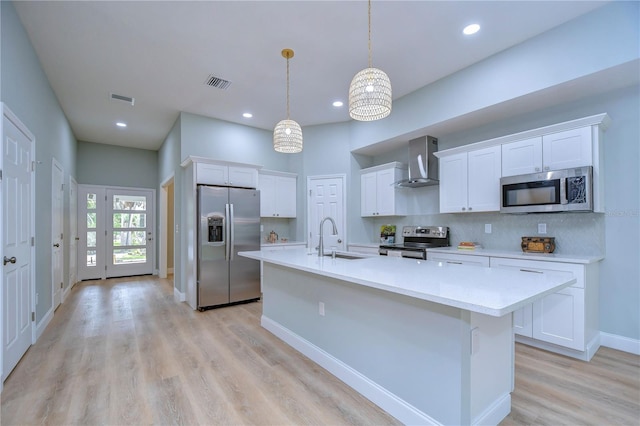 kitchen featuring stainless steel appliances, pendant lighting, white cabinetry, and wall chimney range hood