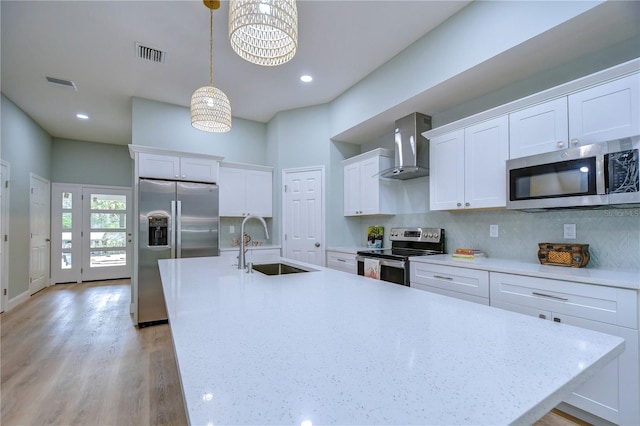 kitchen with white cabinets, decorative light fixtures, wall chimney range hood, stainless steel appliances, and tasteful backsplash