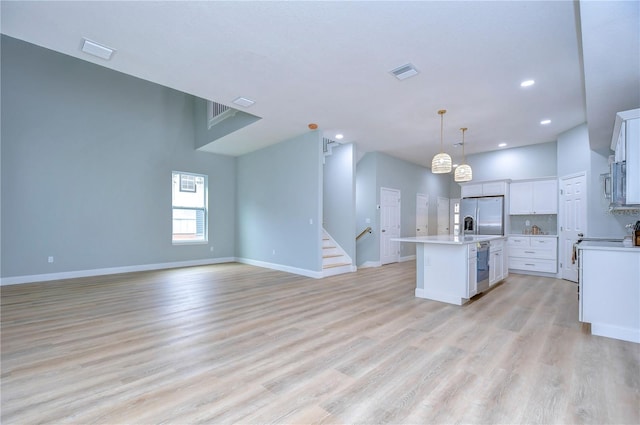 kitchen with light hardwood / wood-style floors, an island with sink, stainless steel appliances, pendant lighting, and white cabinets