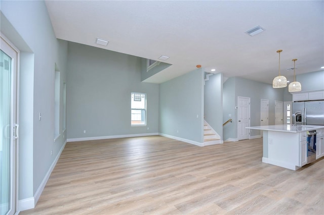 kitchen with stainless steel fridge, a center island with sink, decorative light fixtures, light wood-type flooring, and sink