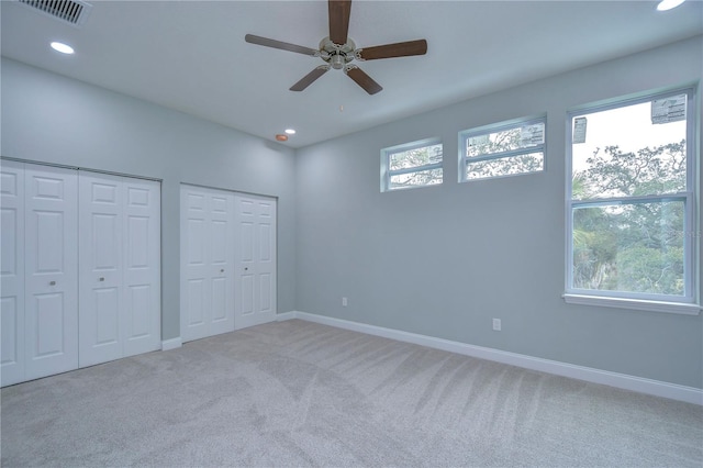 unfurnished bedroom featuring ceiling fan, light colored carpet, and multiple closets