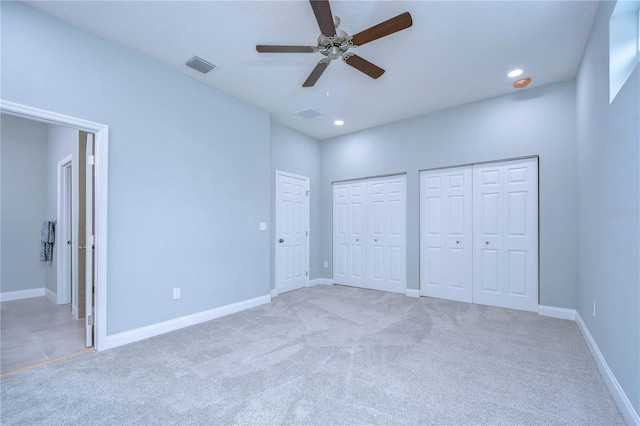 unfurnished bedroom featuring ceiling fan, light colored carpet, and two closets