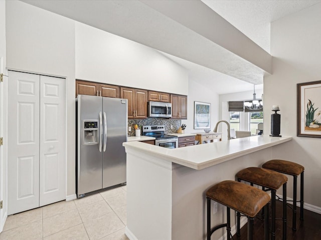 kitchen featuring decorative light fixtures, stainless steel appliances, backsplash, kitchen peninsula, and a breakfast bar