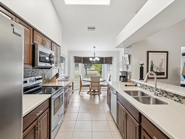 kitchen featuring pendant lighting, appliances with stainless steel finishes, a textured ceiling, tasteful backsplash, and sink