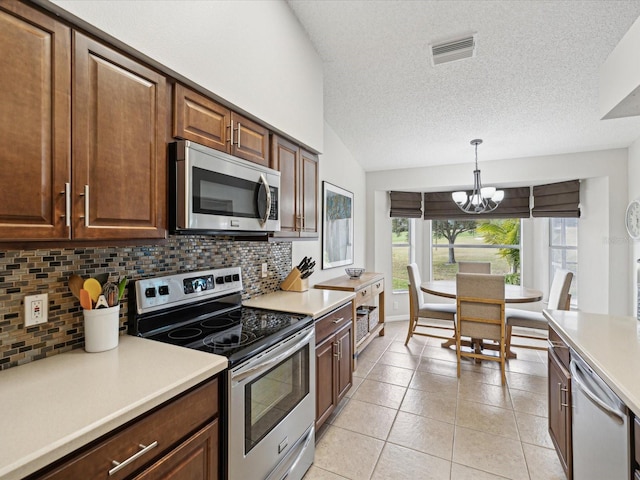 kitchen with appliances with stainless steel finishes, an inviting chandelier, backsplash, hanging light fixtures, and light tile patterned flooring