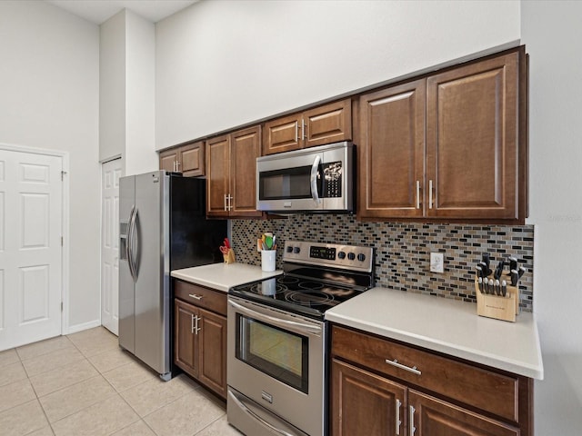 kitchen featuring a high ceiling, appliances with stainless steel finishes, backsplash, light tile patterned floors, and dark brown cabinets