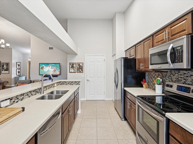 kitchen featuring sink, tasteful backsplash, a towering ceiling, light tile patterned floors, and stainless steel appliances