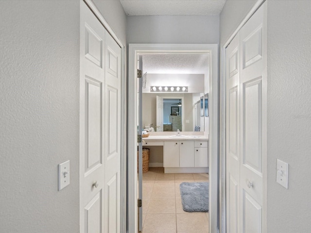 corridor featuring sink, a textured ceiling, and light tile patterned flooring